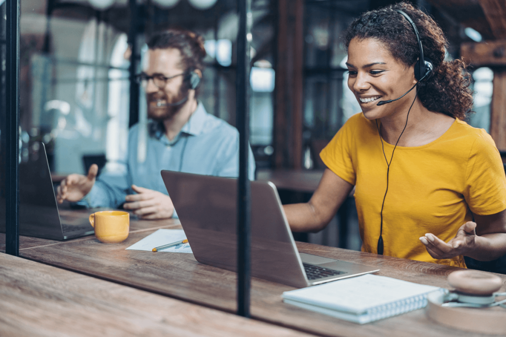 Deux personnes travaillent dans un bureau moderne, séparées par une cloison en verre. Elles sont engagées dans des activités de téléphonie professionnelle.